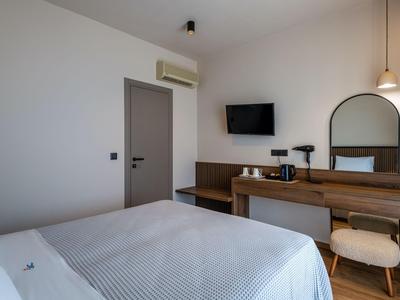 Modernes Hotelzimmer mit großem Bett, Wandfernseher und Schreibtisch mit Stuhl und Hocker.