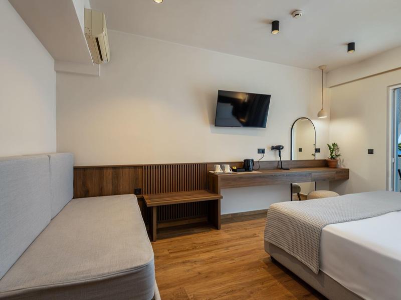 Modernes Hotelzimmer mit Doppelbett, Badezimmerspiegel, Wand-TV und Holzmöbeln mit hellen Farbtönen.