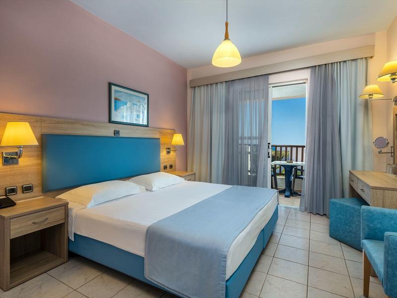 Modernes Hotelzimmer mit Doppelbett, blauen Akzenten, Balkon und Meerblick bei Tageslicht.