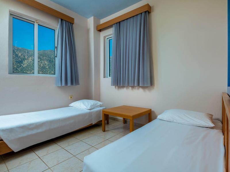 Kleines Schlafzimmer mit zwei Einzelbetten, blau-grauen Vorhängen und kleinem Holztisch.