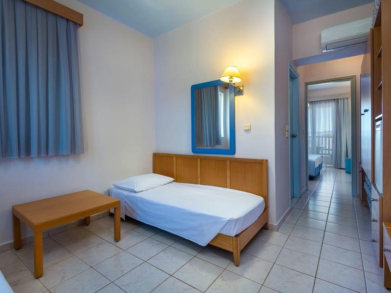 Einzelbettzimmer mit Holzmöbeln, blauem Vorhang und Fliesenboden, langer Flur mit Türen.