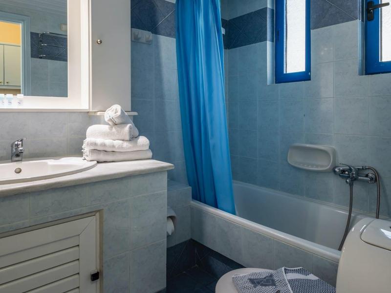 Kleines Badezimmer mit blauem Duschvorhang, Badewanne, Waschbecken und Toilette. Handtücher liegen bereit.