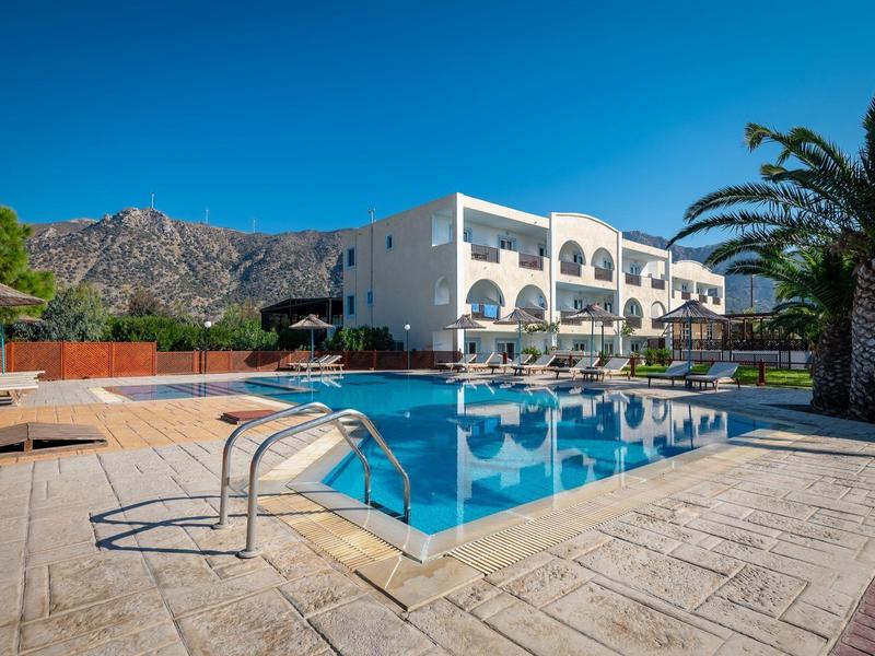 Moderner weißer Bau mit Balkon, großer Pool, Palmen und Bergen im Hintergrund bei klarem Himmel.