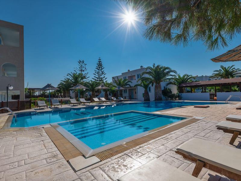 Ein sonniger Außenpool mit Liegestühlen, Palmen und einem klaren blauen Himmel im Hintergrund.