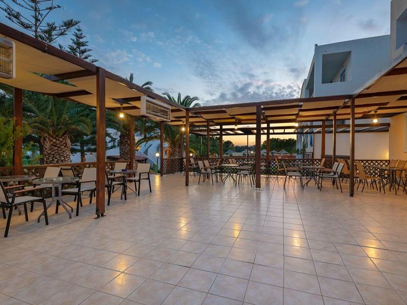 Große, helle Terrasse mit Tischen und Stühlen, überdacht durch Holzkonstruktionen bei Abenddämmerung.