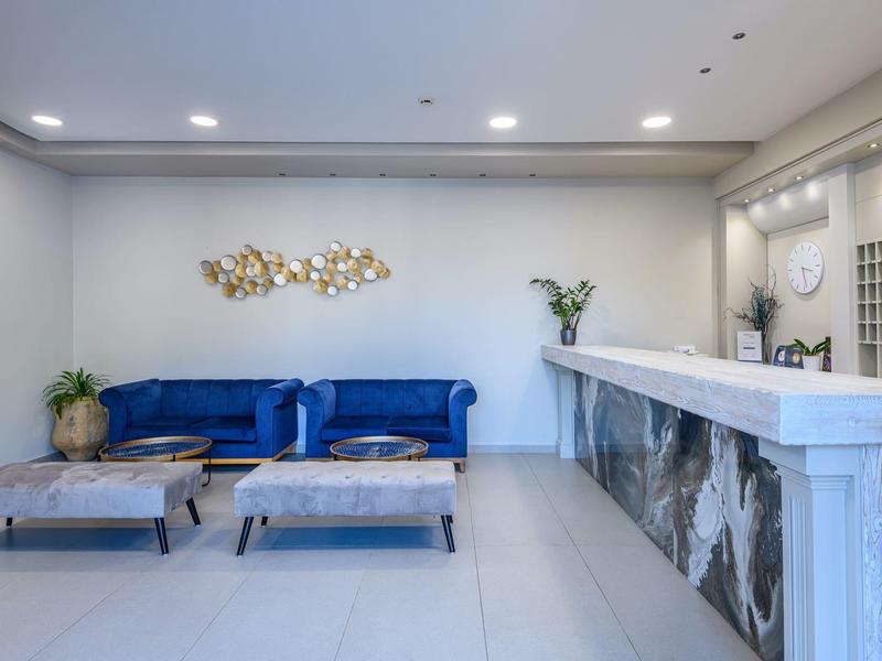 Moderner Wartebereich mit blauem Sofa, zwei Hockern, weißem Tresen und heller Wanddekoration.