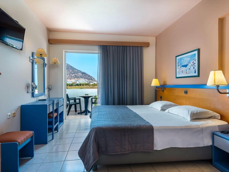 Hell eingerichtetes Hotelzimmer mit Doppelbett, Balkon, Bergblick und Fernseher an der Wand.