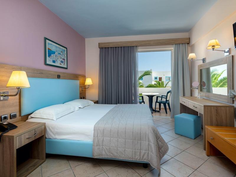 Helles Hotelzimmer mit Doppelbett, Nachttischen, Schreibtisch, Balkon und Blick ins Grüne.