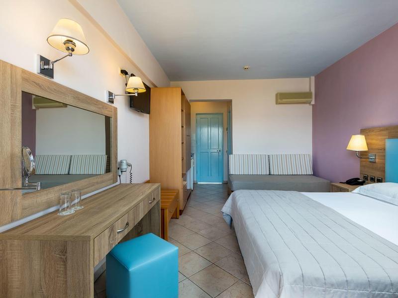 Modernes Schlafzimmer mit Doppelbett, großem Spiegel, Holzkommode und blauem Sitzhocker.