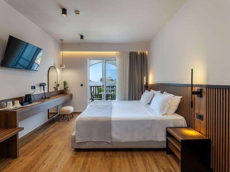 Modernes Schlafzimmer mit Doppelbett, Holzdetails, Fernseher an Wand, Schreibtisch und Balkon mit Sicht nach draußen.