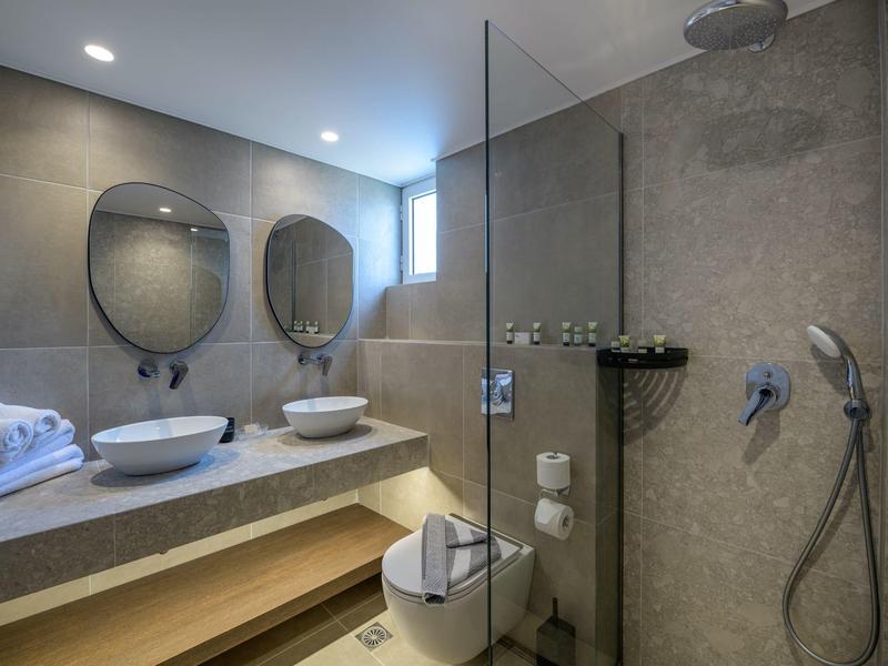 Modernes Badezimmer mit zwei runden Waschbecken, Glas-Dusche und grauen Fliesen an Wand und Boden.