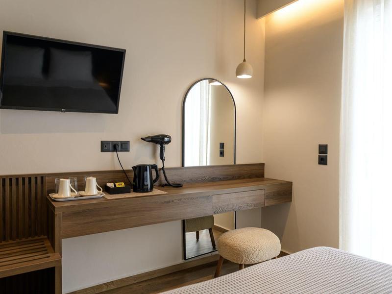 Moderner Hotelzimmerbereich mit Wand-TV, Holzkonsole, Spiegel, Hocker und Teekocher in heller Gestaltung.