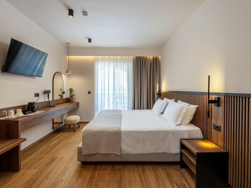 Modernes Hotelzimmer mit Doppelbett, Holzfußboden, Wand-TV und großem Fenster mit Gardinen.