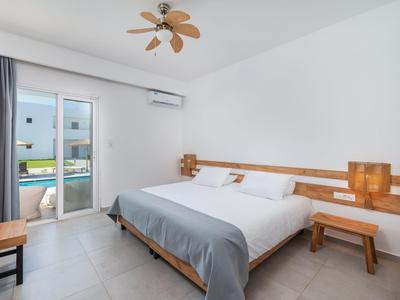 Chambre lumineuse avec grand lit, meubles en bois et accès balcon avec vue sur la piscine.