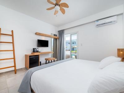 Chambre d'hôtel lumineuse avec grand lit, ventilateur de plafond et accès à un balcon.