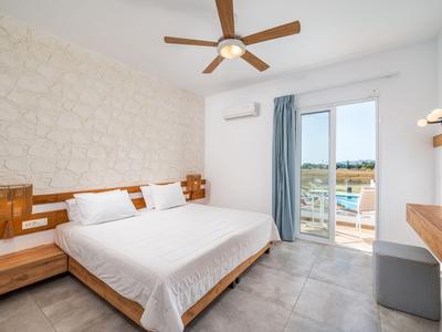 Chambre d'hôtel moderne avec lit double, mur d'accent en pierre claire et balcon avec vue sur la mer.