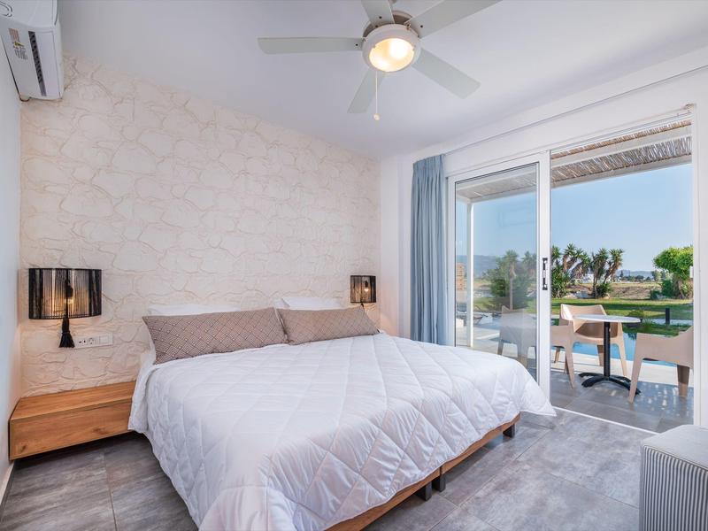 Camera moderna con letto grande, comodini, ventilatore a soffitto e terrazza con vista sull'acqua.