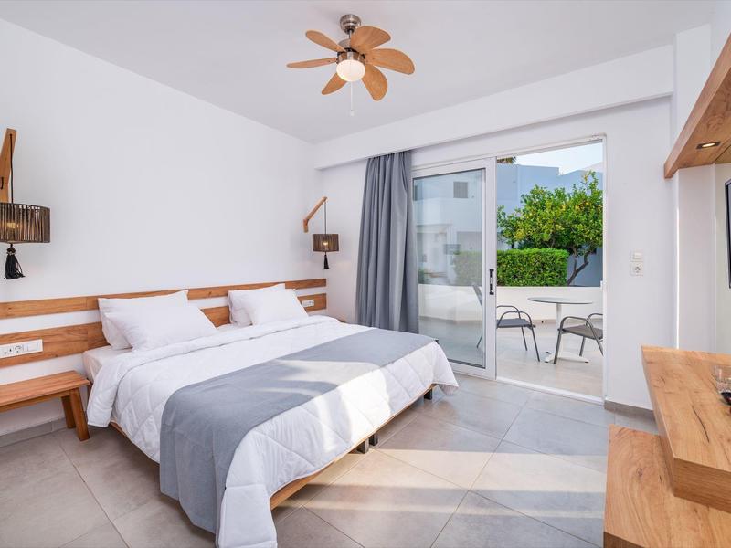 Camera d'hotel moderna con letto matrimoniale, mobili in legno e terrazza con vista sul verde.