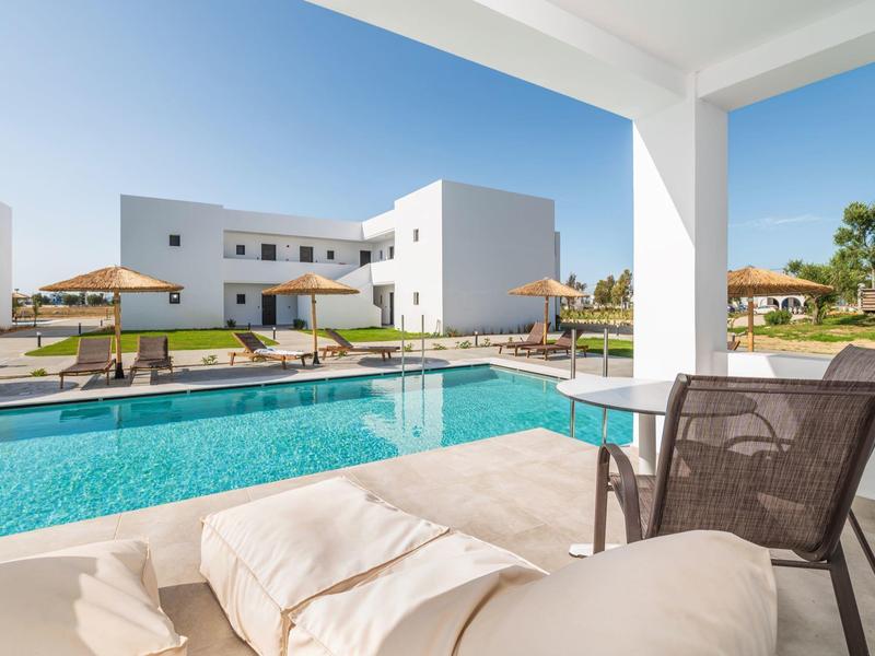 Piscina moderna dell'hotel con lettini e ombrelloni, circondata da edifici bianchi.