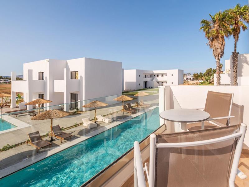 Complesso alberghiero bianco moderno con piscina e area salotto sul balcone sotto un cielo limpido.