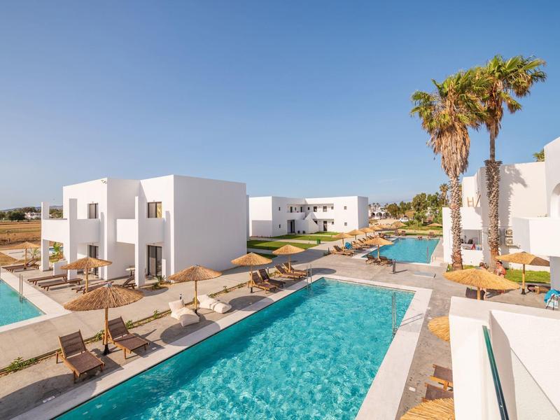 Complesso alberghiero moderno con più piscine, lettini e palme sotto un cielo limpido.