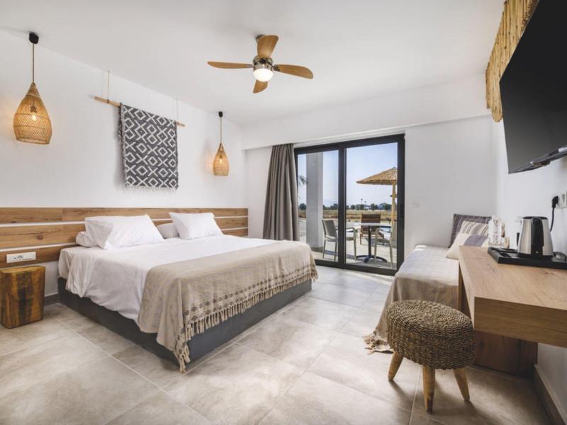 Camera d'hotel luminosa con letto matrimoniale, ventilatore a soffitto, balcone e scrivania con TV.