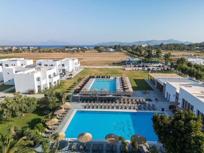 Complesso alberghiero moderno con due piscine e lettini in un ambiente rurale sotto un cielo sereno.