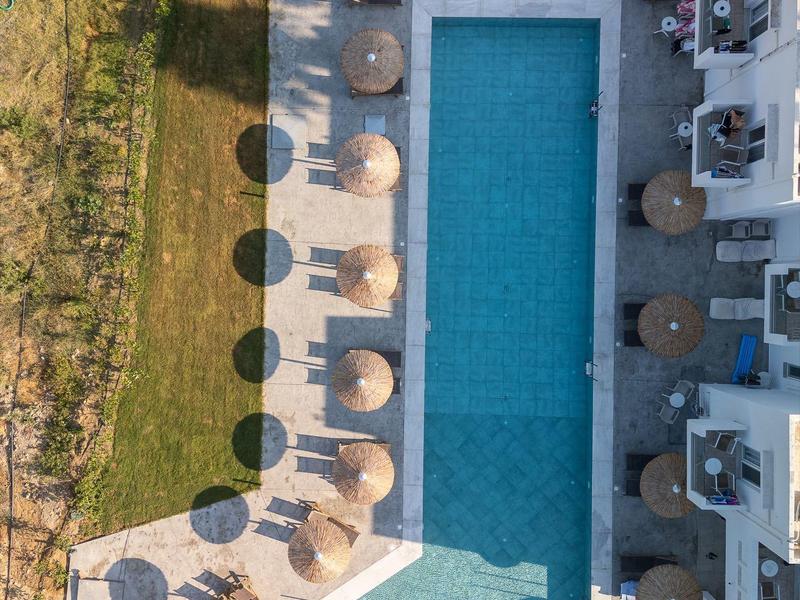 Vista drone di una piscina rettangolare con ombrelloni e sdraio accanto a un edificio.