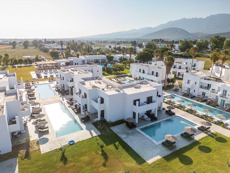 Moderno complesso turistico con più edifici bianchi e due grandi piscine in un paesaggio soleggiato.