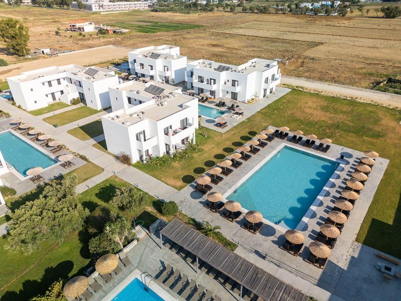 Veduta aerea di un resort con più edifici bianchi, piscine e ombrelloni in campagna.
