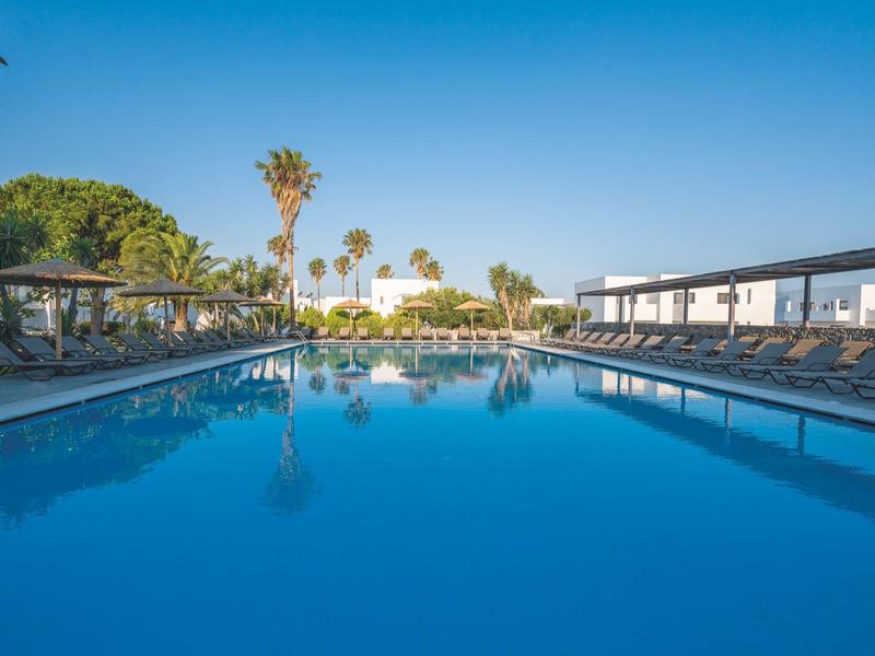 Piscina limpida con lettini e palme in un'area dell'hotel sotto un cielo blu.
