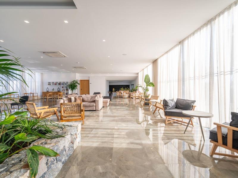 Zona lounge di un hotel moderna e luminosa con grandi finestre e piante.