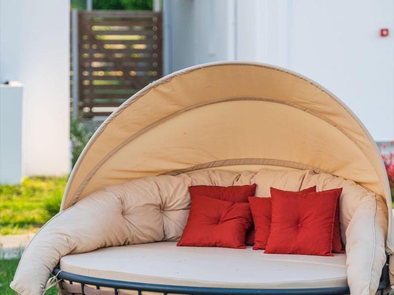 Lettino tondo in vimini con tenda beige e cuscini rossi su prato