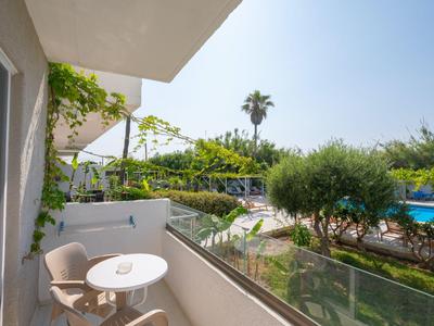 Balcone con tavolo e sedie, vista su giardino e piscina, cielo soleggiato.