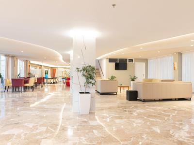 Ampia e luminosa hall dell'hotel con poltrone moderne, piante e pavimento in marmo.