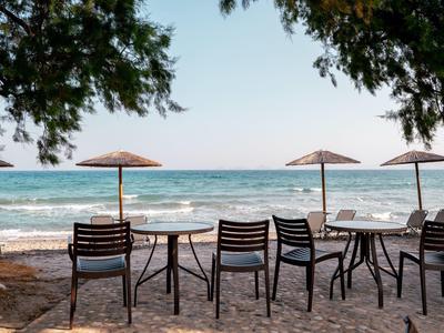 Sedie e tavoli vuoti sotto ombrelloni sulla spiaggia con vista sul mare.