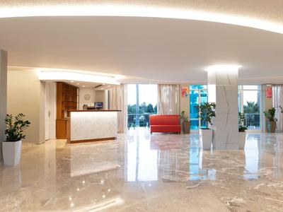 Lobby dell'hotel luminosa con pavimento in marmo, reception e area salotto con divani rossi.