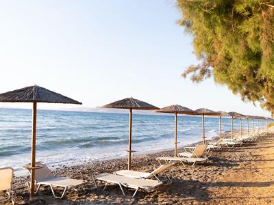 Lettini vuoti e ombrelloni sulla spiaggia con mare calmo e cielo sereno.