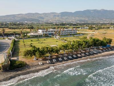 Spiaggia con sdraio e strada vicina, circondata da campi verdi e montagne sullo sfondo.