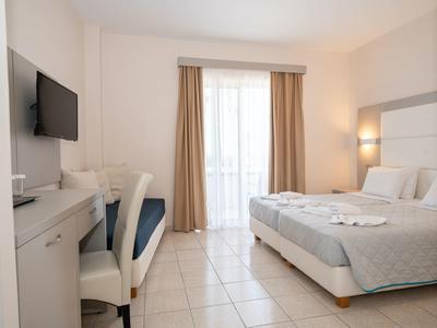 Camera d'hotel luminosa con letto matrimoniale, scrivania, TV e balcone con tende.