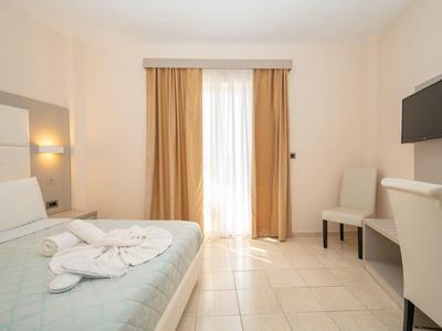 Camera d'hotel luminosa con letto azzurro chiaro, tende marroni e TV a parete.