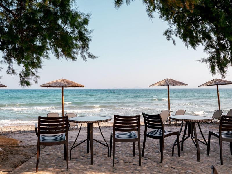 Sedie e tavoli vuoti sotto ombrelloni sulla spiaggia con vista sul mare.