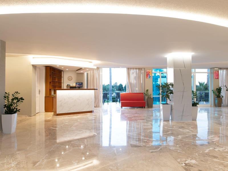 Reception luminosa con pavimento in marmo lucido e zona salotto con divani rossi.