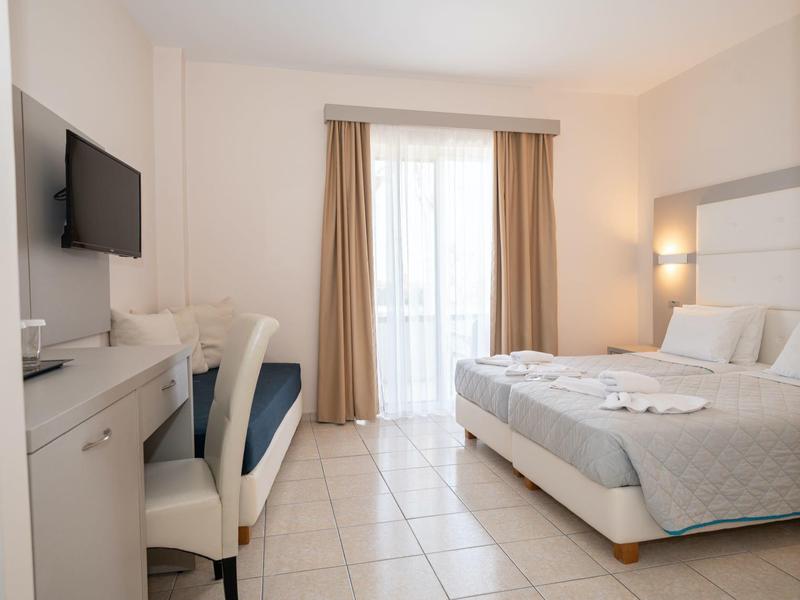 Camera d'hotel luminosa con letto matrimoniale, scrivania, TV e balcone con tende.