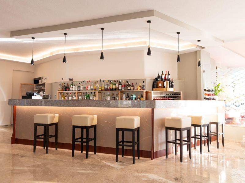 Area bar moderna dell'hotel con legno chiaro, sgabelli e illuminazione indiretta.