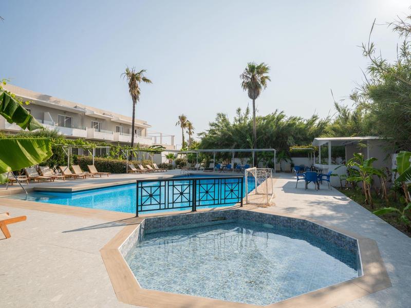 Area piscina dell'hotel con ombrelloni, lettini e vegetazione tropicale sotto un cielo limpido