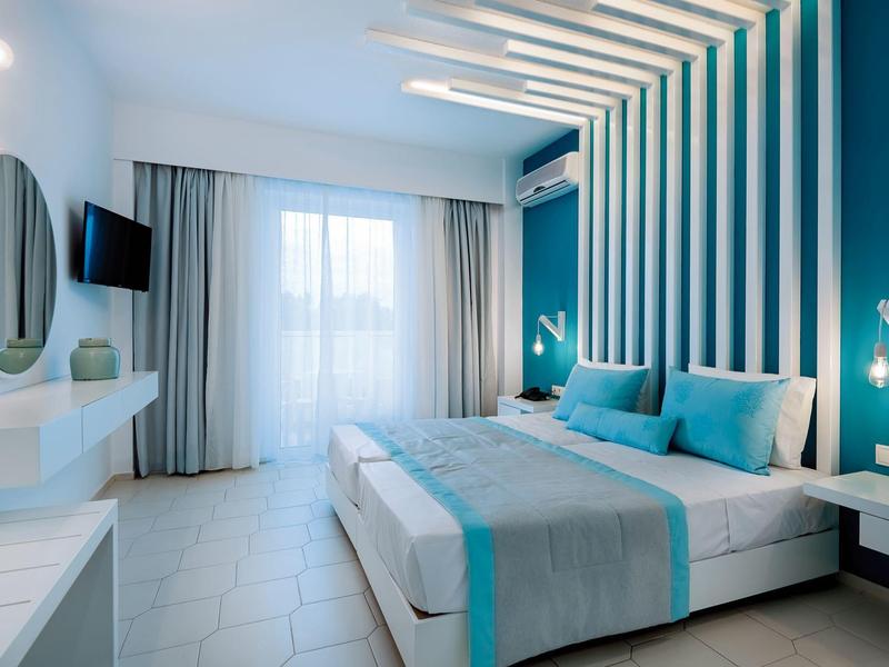 Nowoczesny pokój hotelowy z podwójnym łóżkiem, turkusowymi akcentami i dużym oknem.
