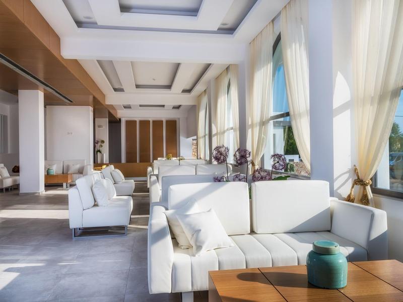 Jasny salon hotelowy z dużymi oknami, białymi sofami i nowoczesnym wystrojem.