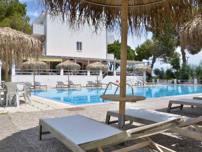 Pohled na hotelový bazén s lehátky a slámovými slunečníky v zahradě.