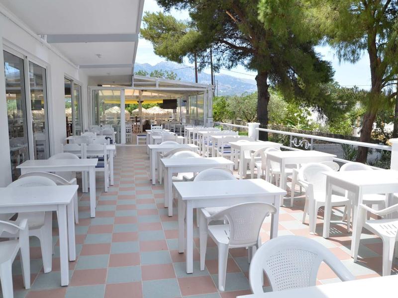 Terasa s bílými plastovými židlemi a stolky pod stromy s výhledem na moře.